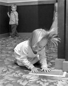 Image of a girl playinig with A/C and a boy watching her at a distance